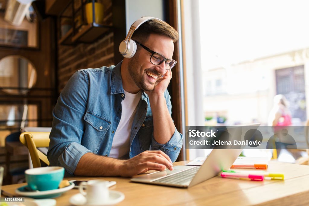 Freelancer at coffee shop Smiling young man listening mujsic at the coffee shop Headphones Stock Photo