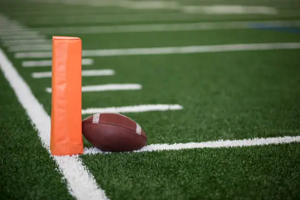Selective focus photo of the pylon and touchdown line on a football field. Low angle view from the end zone in an indoor stadium