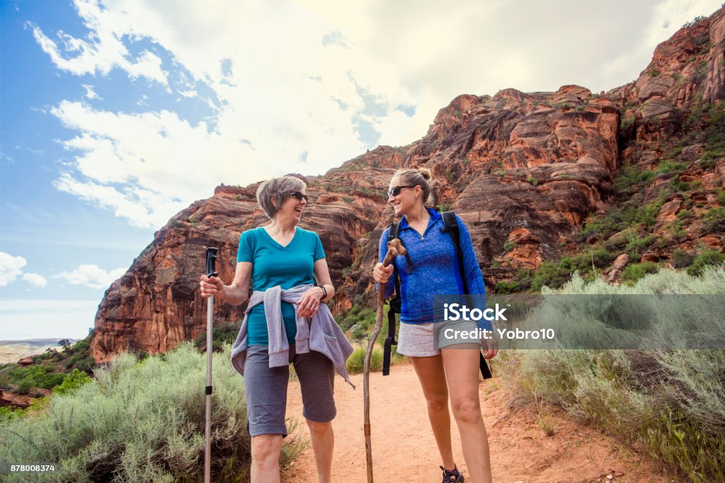 Women hiking together in a beautiful red rock canyon Two happy women hiking together in a red rock sandstone canyon in the deserts of Utah on an adventure vacation. Two women smiling and talking together during a fun hike Hiking Stock Photo