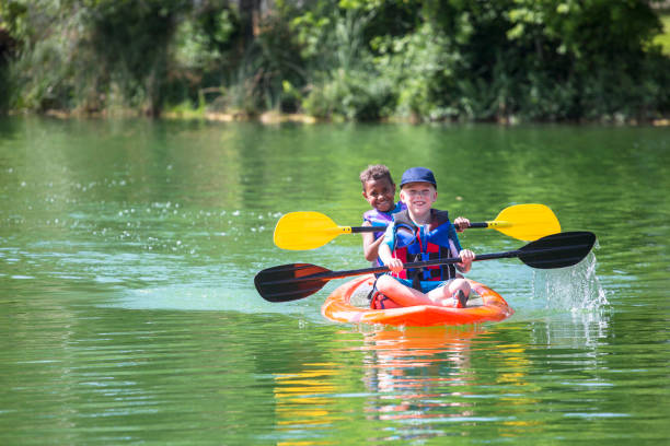 dos diversos niños kayak por un río hermoso - campamento de verano fotografías e imágenes de stock