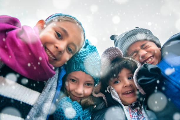 Children Group Hug Group of kids wrapped up in warm clothes hugging outdoors in winter, low point of view. children in winter stock pictures, royalty-free photos & images
