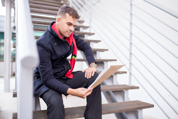 istock Concentrated young man reading papers on stairs 878116018