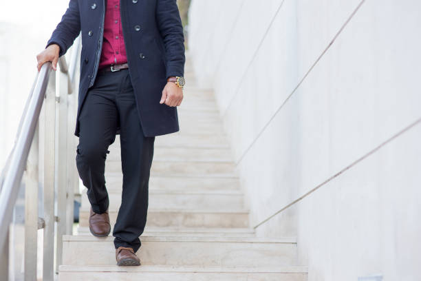 Stylish young Caucasian businessman wearing coat going downstairs outdoors. Business and fashion concept