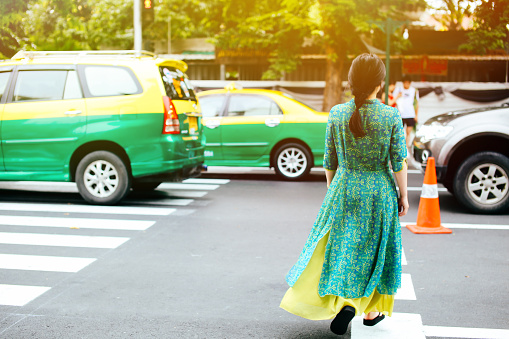 Woman in traditional Asian dress crossing the road in Bangkok, Thailand
