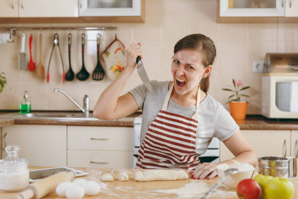 istock A young evil and aggressive woman sitting at a table and attacking the dough with a knife in the kitchen. Cooking home. Prepare food. 878169256