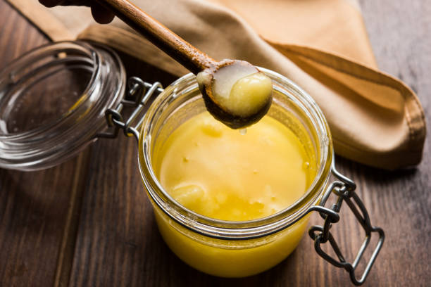 desi pure ghee o burro chiarificato in vetro o contenitore di rame con cucchiaio, messa a fuoco selettiva - butter foto e immagini stock