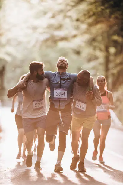 Photo of Male runners carrying injured athlete during marathon race in nature.