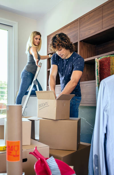 istock Couple unpacking boxes and placing books 878195418