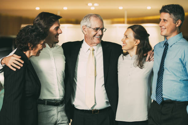 Smiling Senior Business Leader Embracing Coworkers Closeup of smiling senior business man embracing colleagues. They are standing and with blurred view in background. five people photos stock pictures, royalty-free photos & images