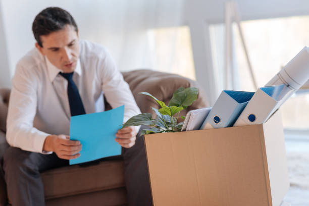 istock Calm elegant man reading a document while sitting in front of a big box 878234986