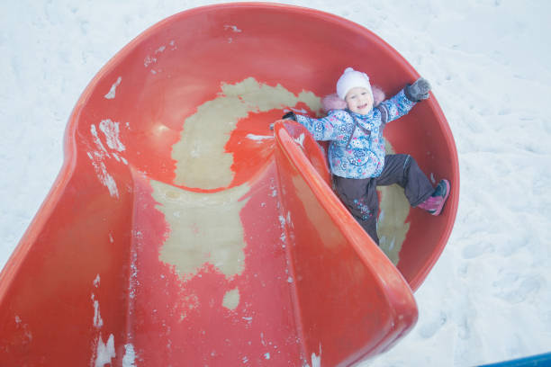 diversão de inverno da menina no slide do campo de jogos plástico vermelho - playground snow winter little girls - fotografias e filmes do acervo