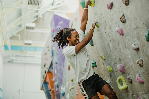 A young athlete guy climbs up a training wall for climbing with many hooks. View from below