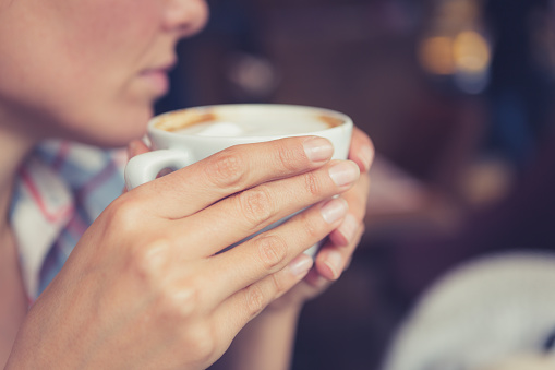 Close up of woman hands holding a cup of coffee, sitting in cafe