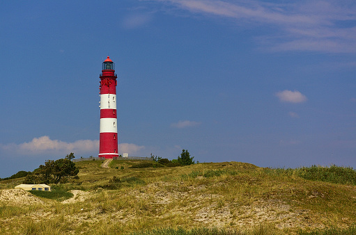 Red and white lighthouse on a sand dune lightly covered with beach grass in front of a blue sky