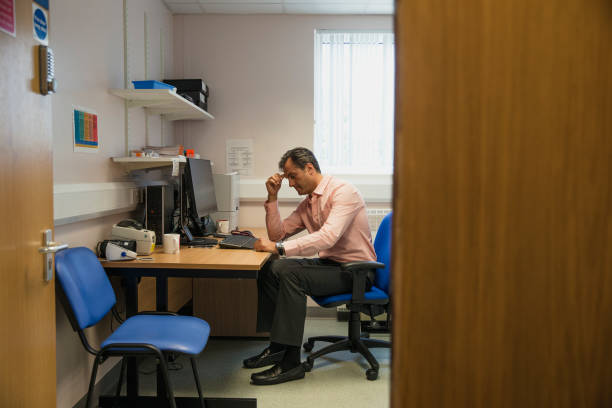 Worried Doctor A doctor sits at his desk looking very worried doctor general practitioner stock pictures, royalty-free photos & images
