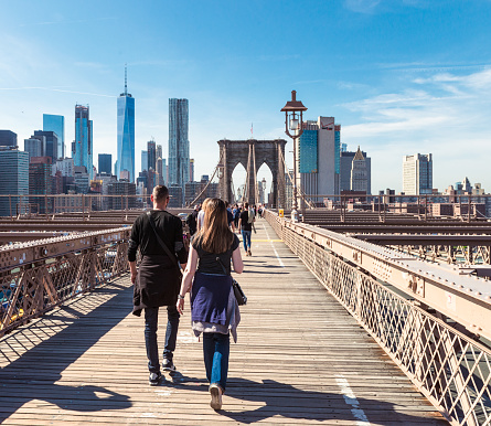 New York City, USA - Rear view of pedestrians walking over Brooklyn Bridge, heading towards Manhattan Island from Brooklyn.