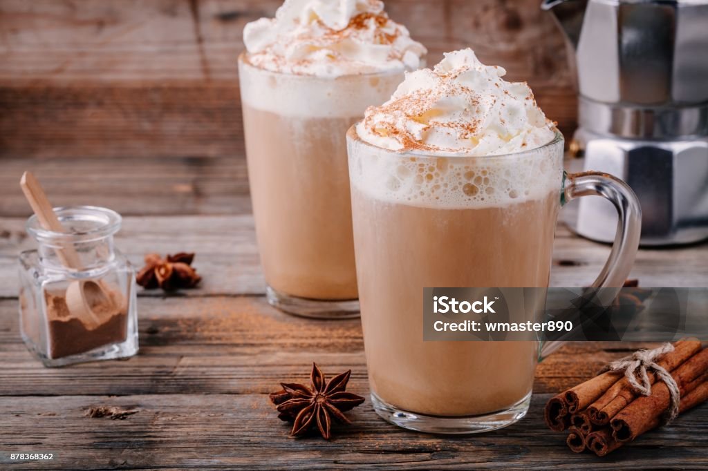 Pumpkin spice latte with whipped cream and cinnamon Pumpkin spice latte with whipped cream and cinnamon in glass on wooden background Latte Stock Photo