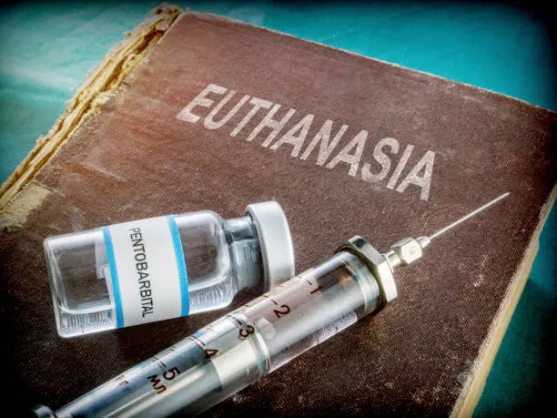 Vial and vintage syringe with medicine on an old book of euthanasia, conceptual image