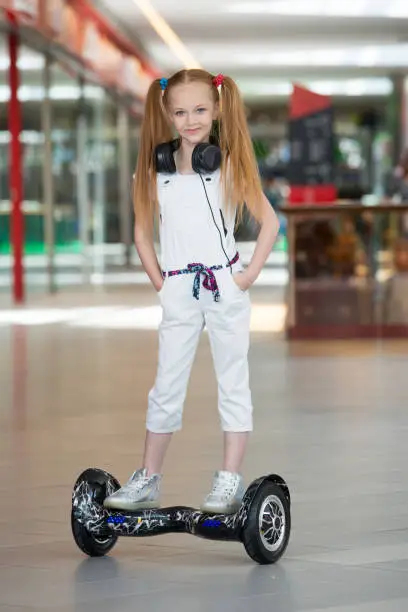 Happy and smiling girl rides on mini segway in the headphones at trading mall. Teenager riding on hover board or gyroscooter and listening to music