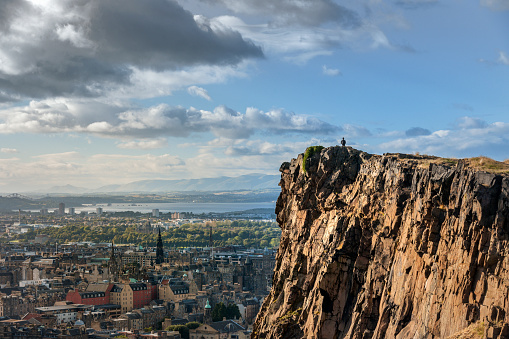 Man looking out over the City of Edinburgh from Salisbury Crags in Holyrood Park at sunset