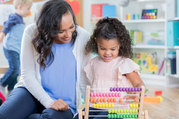 istock Smiling preschool teacher helps student with math 878418226