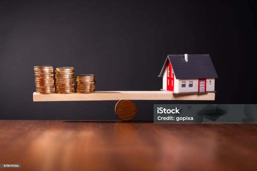 Symbol photo solid construction financing Seesaw with a house on one side and stacks with coins on the other. Stability Stock Photo