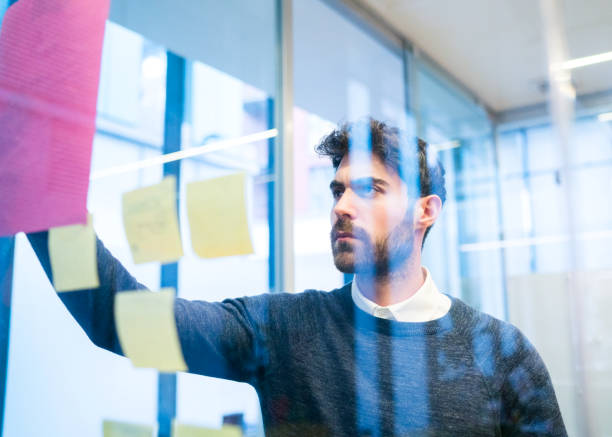 istock Businessman looking at adhesive note on glass wall 878422310