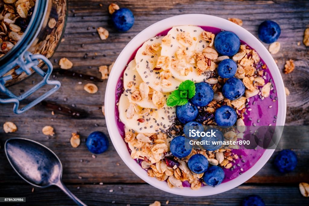 healthy smoothie bowl with granola, banana and fresh blueberries healthy smoothie bowl with granola, banana and fresh blueberries on wooden background Bowl Stock Photo