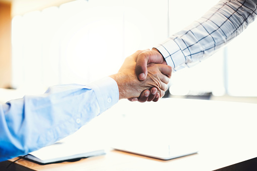 Cropped hands of businessman shaking hands. Mid adult colleagues greeting each other in board room. They are at office.