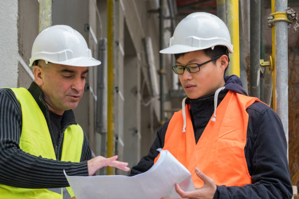 istock Young Asian apprentice at work on construction site with senior engineer. Outdoors 878440954