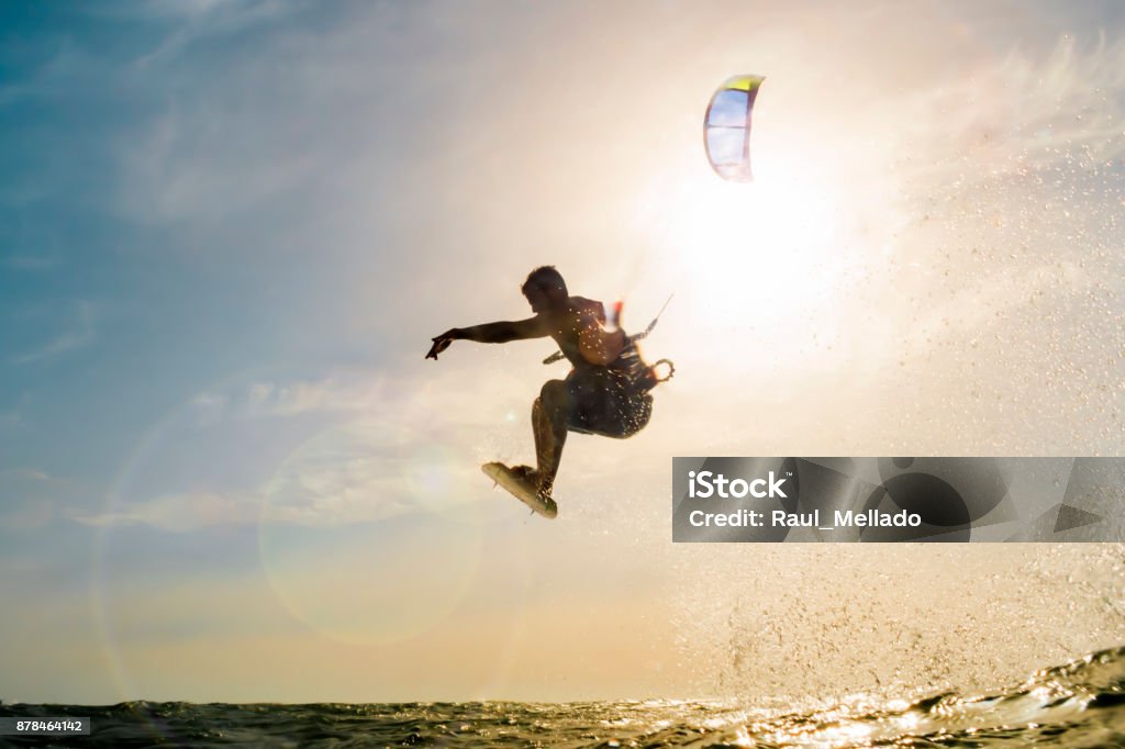 Surfer flying in front of the sunset surfer flying over the golden waters of the sea in front of a beautiful sunset Kiteboarding Stock Photo