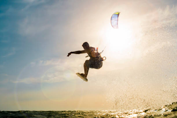 Surfer flying in front of the sunset surfer flying over the golden waters of the sea in front of a beautiful sunset kiteboard stock pictures, royalty-free photos & images