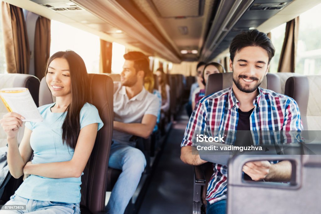 El chico de la camisa se sienta en el autobús y mira algo sobre su tableta gris. Él sonríe. - Foto de stock de Autobús libre de derechos