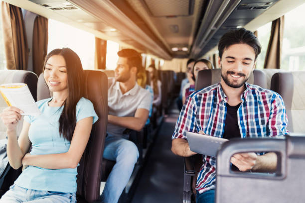 The guy in the shirt sits on the bus and looks at something on his gray tablet. He smiles. stock photo