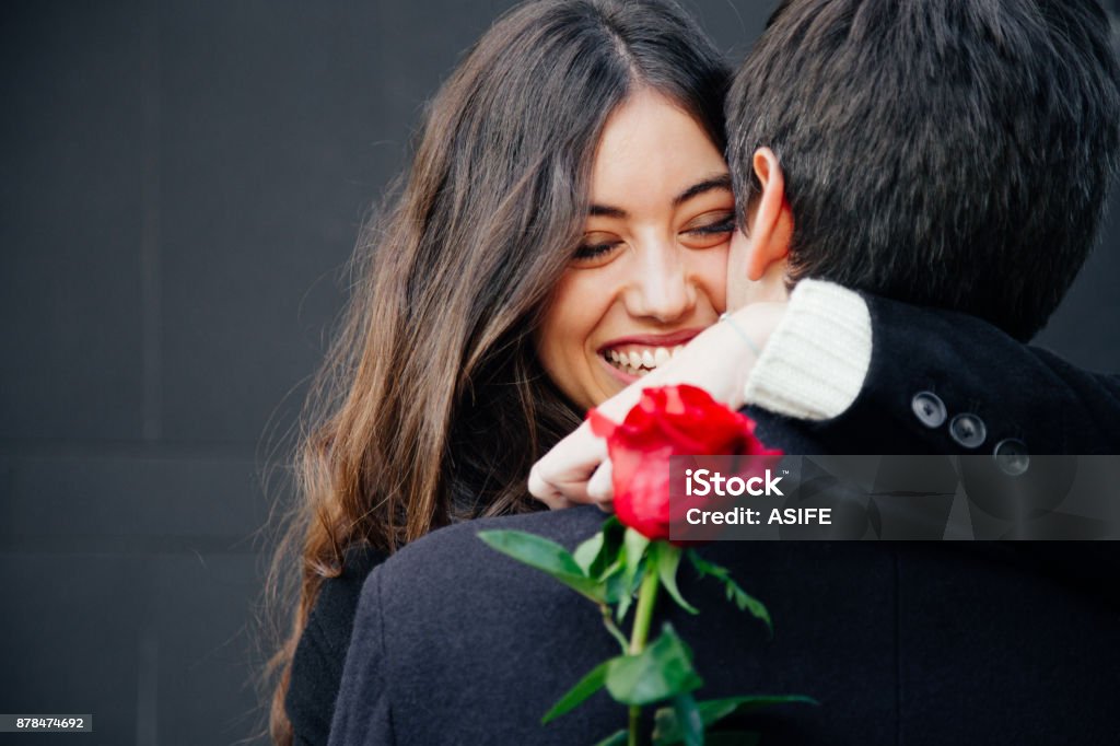 Happy and beautiful couple in love Beautiful and happy young woman in love hugging her boyfriend holding a red rose Valentine's Day - Holiday Stock Photo