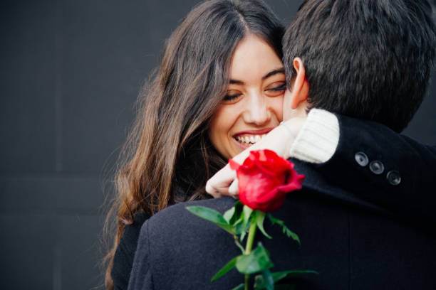 Happy and beautiful couple in love Beautiful and happy young woman in love hugging her boyfriend holding a red rose falling in love photos stock pictures, royalty-free photos & images