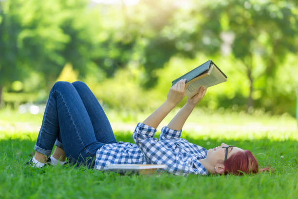 istock Woman lying on green grass reading a book 878478254