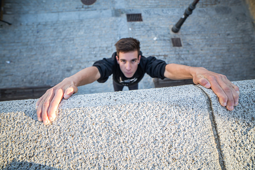 Young man hanging on wall on hands and trying to climb up while doing parkour.