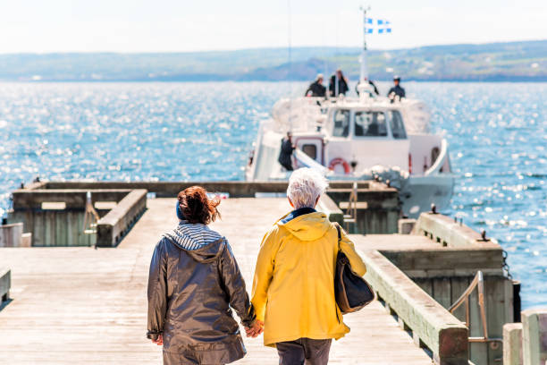 Bonaventure Island Park entrance in Gaspe Peninsula, Quebec, Gaspesie region with senior couple woman holding hands walking to boat ferry on dock pier Perce: Bonaventure Island Park entrance in Gaspe Peninsula, Quebec, Gaspesie region with senior couple woman holding hands walking to boat ferry on dock pier gaspe peninsula stock pictures, royalty-free photos & images