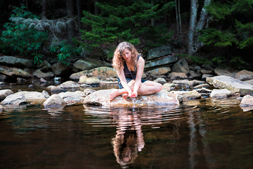 Young woman enjoying nature on peaceful, calm Red Creek river in Dolly Sods, West Virginia during sunny day with reflection dipping hands in water to drink fresh, splashing