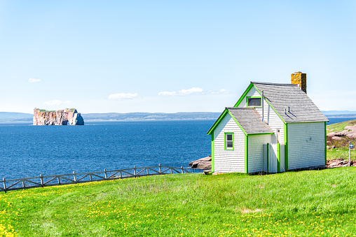 View of Rocher Perce rock and arch from Bonaventure Island with ocean and green wooden painted house, coastline