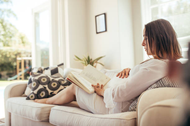 istock Pregnant woman relaxing on sofa reading  book 878578912