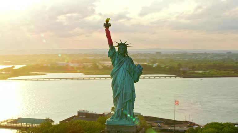 AERIAL Statue of Liberty on Liberty Island at sunset with NYC in the background