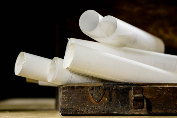 istock Old rolls and plans in folded paper rolls. Old book and case. Documents on an old wooden table. Black background. 878626838