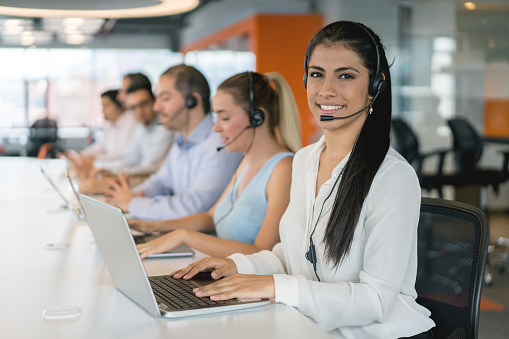 Group of people working at a call center wearing headsets and looking very happy