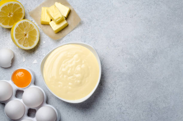 Basic french sauce hollandaise in a white bowl with ingredients, Homemade basic french sauce hollandaise in a white bowl with ingredients, butter, lemon, eggs, on a light blue slate stone background with copy space, top view hollandaise sauce stock pictures, royalty-free photos & images