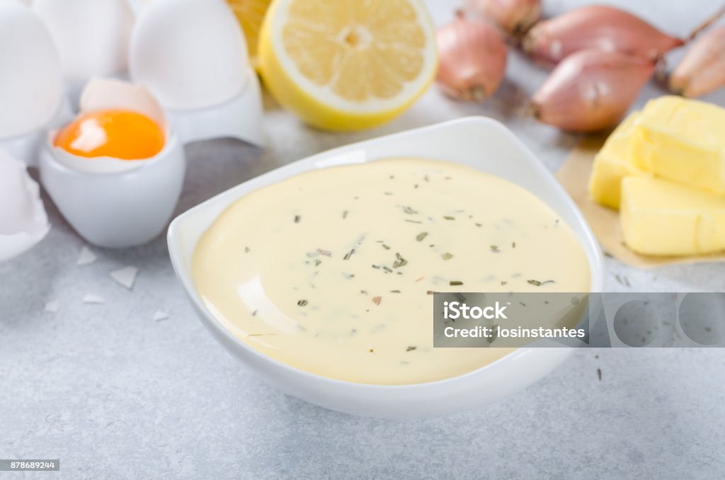 Basic french sauce bearnaise in a white bowl with ingredients, b Homemade basic french sauce bearnaise in a white bowl with ingredients, butter, shallot, lemon, eggs, on a light blue stone background, close-up Butter Stock Photo