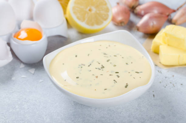Basic french sauce bearnaise in a white bowl with ingredients, b Homemade basic french sauce bearnaise in a white bowl with ingredients, butter, shallot, lemon, eggs, on a light blue stone background, close-up hollandaise sauce stock pictures, royalty-free photos & images