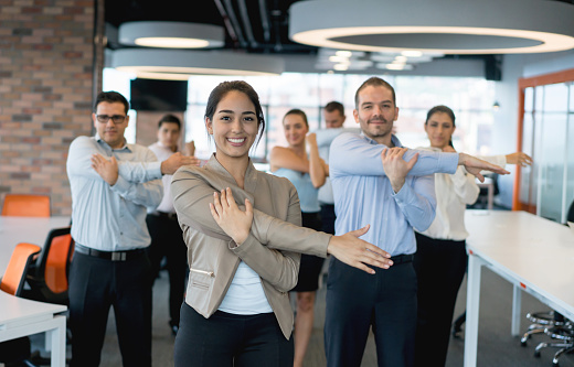 Happy group of business people stretching while taking a break from work at the office â wellbeing concepts