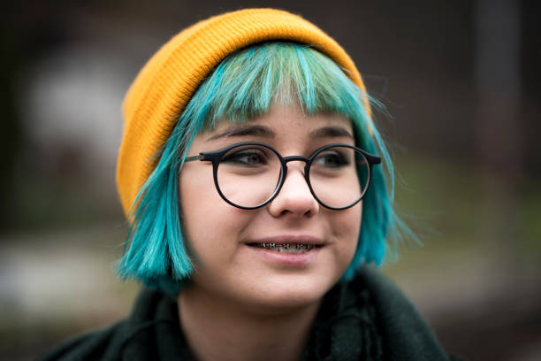 Young hipster girl with green hair, yellow cap and eyeglasses smiling and looking away.